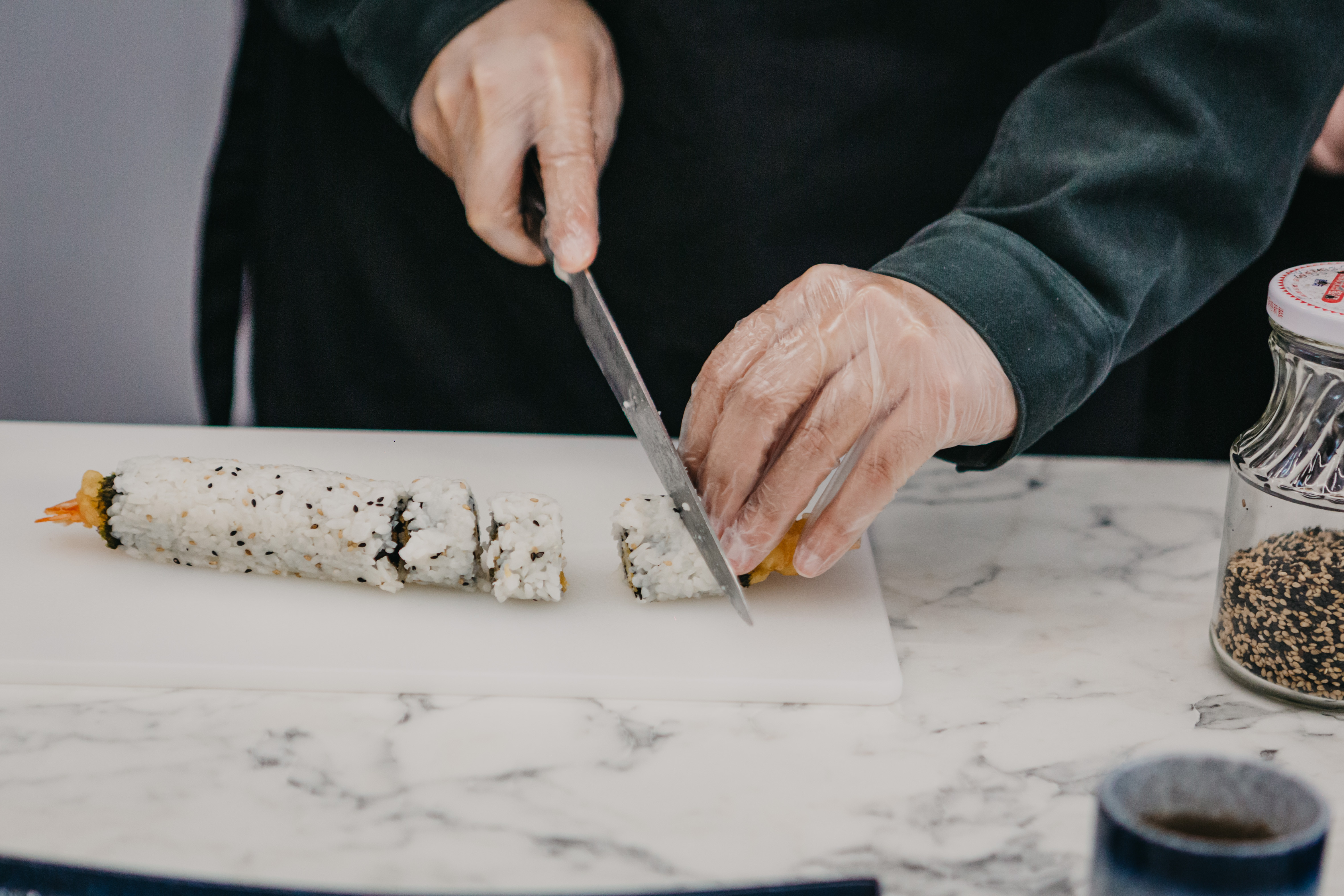 A person slicing a long sushi roll into smaller portions